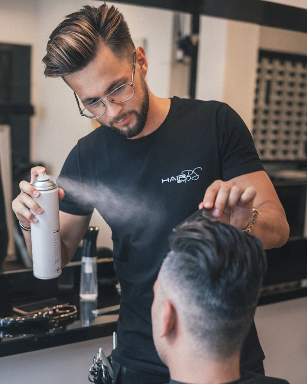 Rafael Moura, barbeiro, finalizando um corte degradê com spray fixador