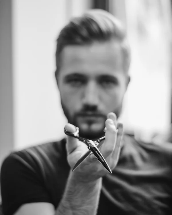 Thiago Nunes, barbeiro, em retrato preto e branco segurando uma tesoura